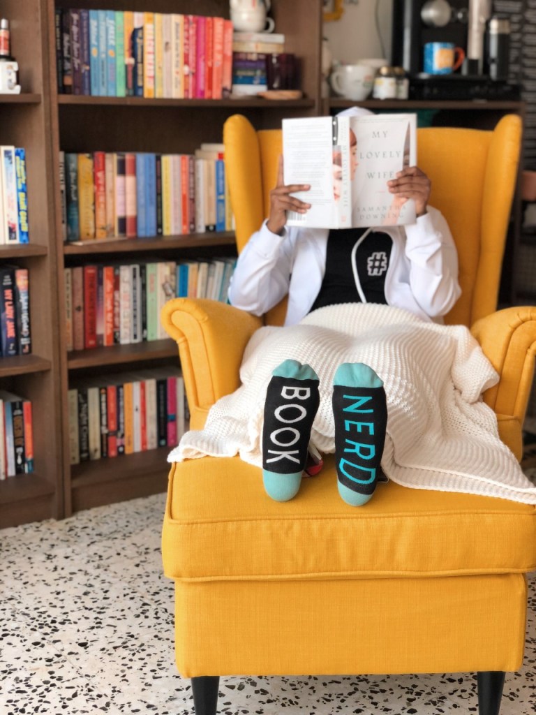 Nada sitting on a yellow chair holding up a book showing socks with book nerd written on them and a book library in the background